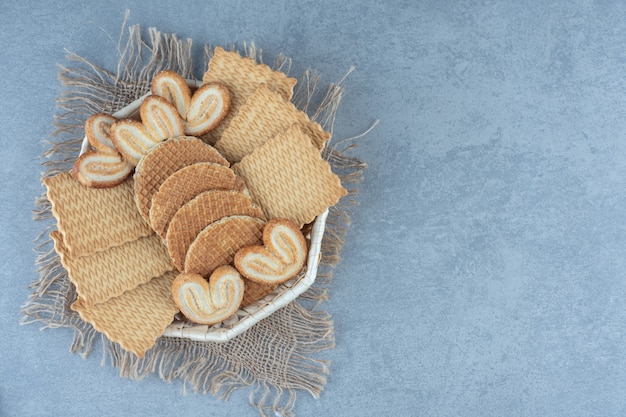 Vari tipi di biscotti e cialde in cestino sul sacco sopra il tavolo grigio.