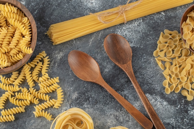 Vari tipi di pasta cruda con cucchiai di legno.