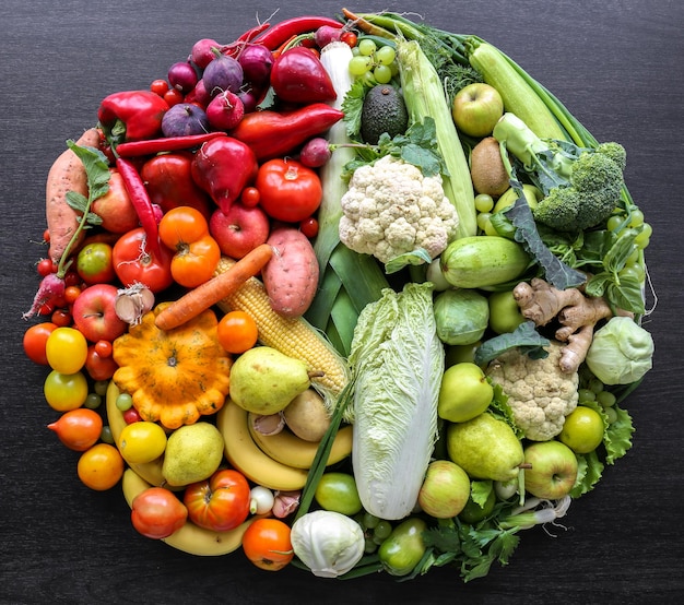 Varie verdure e frutta disposte in cerchio su uno sfondo scuro