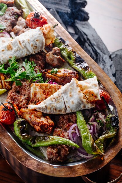 Varietà di kebab con verdure all'interno del piatto di legno.