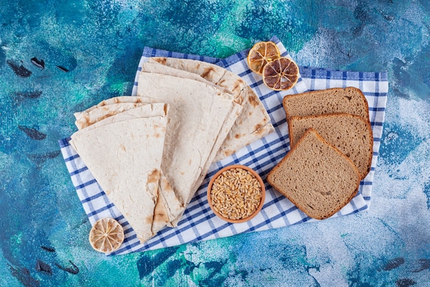 Varietà di pane fragrante fresco con ciotola di orzo sulla superficie blu.