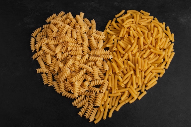 Varietà di pasta a forma di cuore su superficie nera.