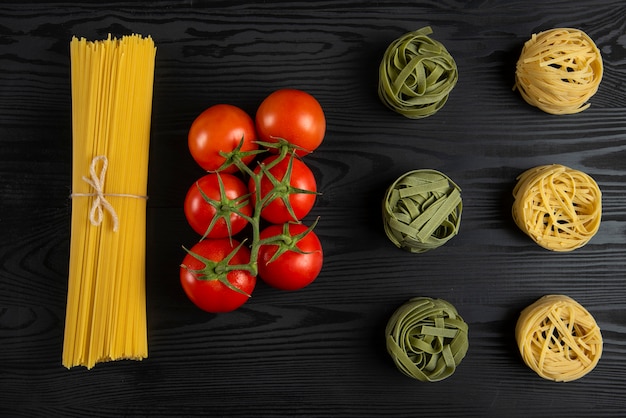 Varietà di pasta italiana con pomodori sul tavolo nero
