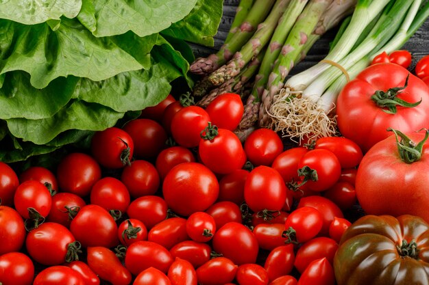 Varietà di pomodori con lattuga, asparagi, cipolle verdi close-up su una parete di legno