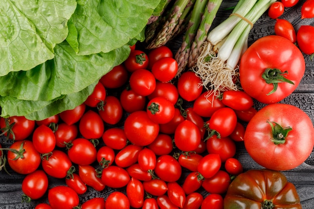 Varietà di pomodori con lattuga, asparagi, cipolle verdi sulla parete di legno, piatto disteso.