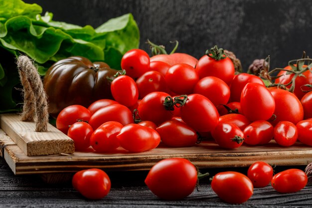 Varietà di pomodori in un vassoio fatto a mano con vista laterale di lattuga sul muro di legno e scuro