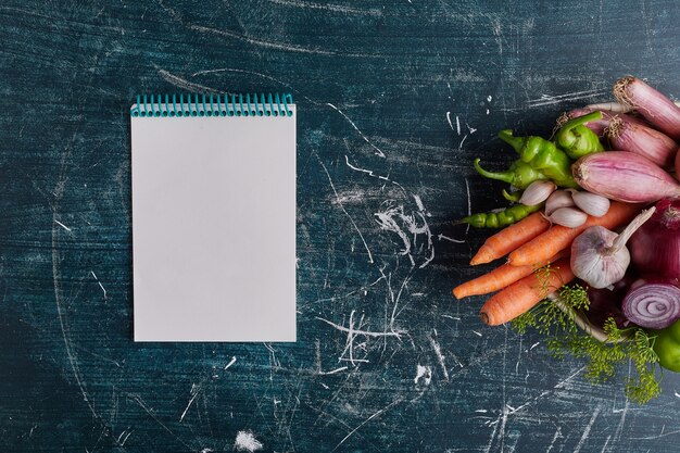 Varietà di verdure isolate sul tavolo blu sul lato destro con un ricettario da parte.