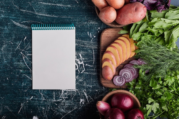 Varietà di verdure isolate sulla tavola blu con un libro di ricette da parte.