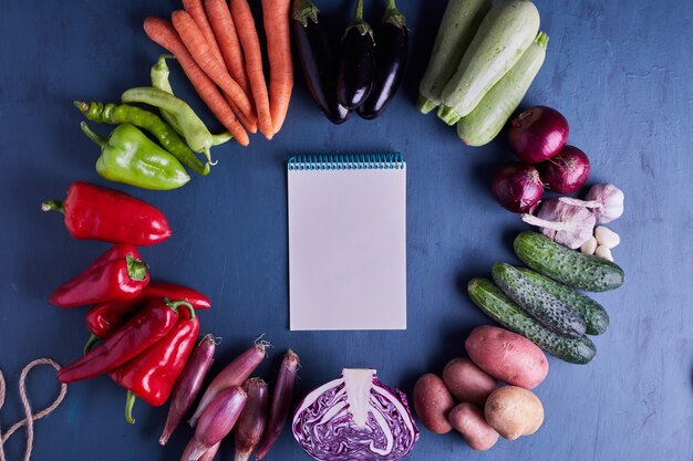 Varietà di verdure isolate sulla tavola blu con un libro di ricette nel mezzo.