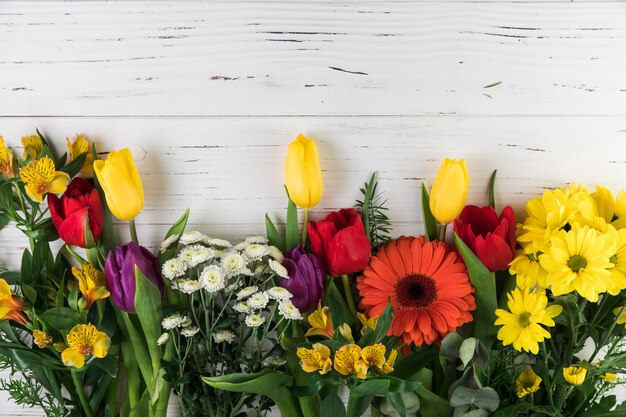 Vario bouquet di fiori colorati decorato su fondo di legno bianco