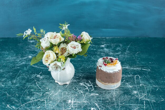 Vaso con fiori bianchi e una piccola torta su blu.