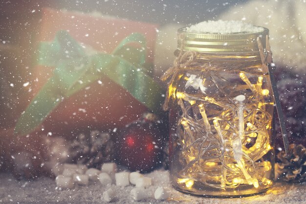 vaso di cristallo con le luci con un regalo accanto ad essa, mentre nevica