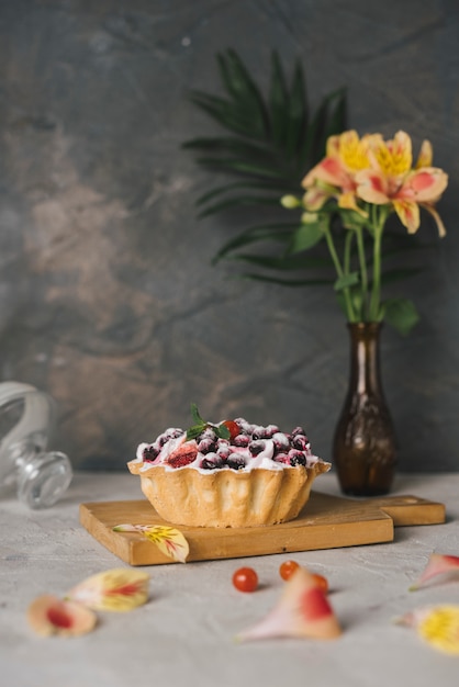 Vaso di fiori Alstroemeria vicino alla gustosa torta di frutti di bosco sul tagliere