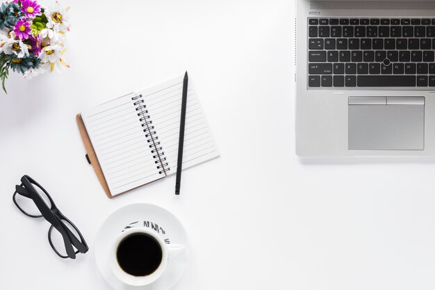 Vaso di fiori; occhiali; diario; tazza di caffè e matita con il computer portatile su priorità bassa bianca