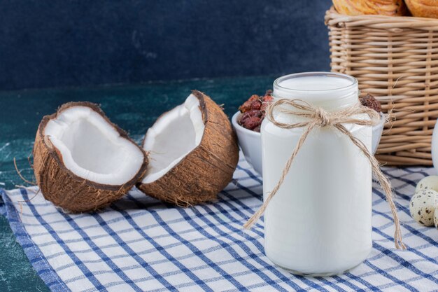 Vaso di vetro di latte e noci di cocco tagliate a metà sul tavolo di marmo.