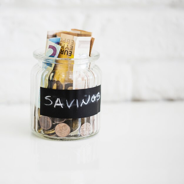 Vaso di vetro di risparmio con banconote e monete in euro su sfondo bianco