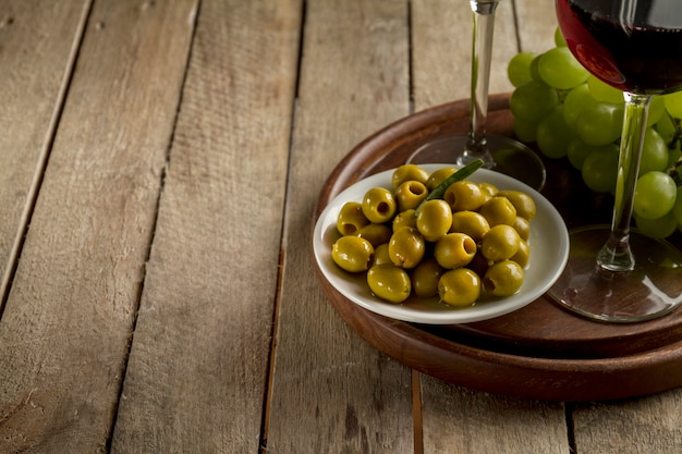 Vassoio in legno con olive, uva e bicchieri di vino