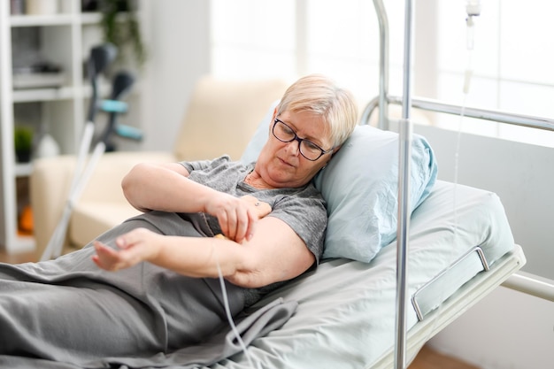 Vecchia donna caucasica in pensione coperta da una coperta in una casa di cura che controlla la sua trasfusione.