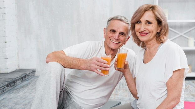 Vecchie coppie felici che si siedono a casa tenendo vetro di succo