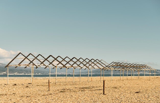 Vecchie tettoie dal sole su una spiaggia di ciottoli della città Costa del Mar Nero vuota spiaggia calma in una giornata di sole Il cielo è bruciato a mezzogiorno baia del mare e sullo sfondo ci sono le montagne del Caucaso Campioni pastello calmanti