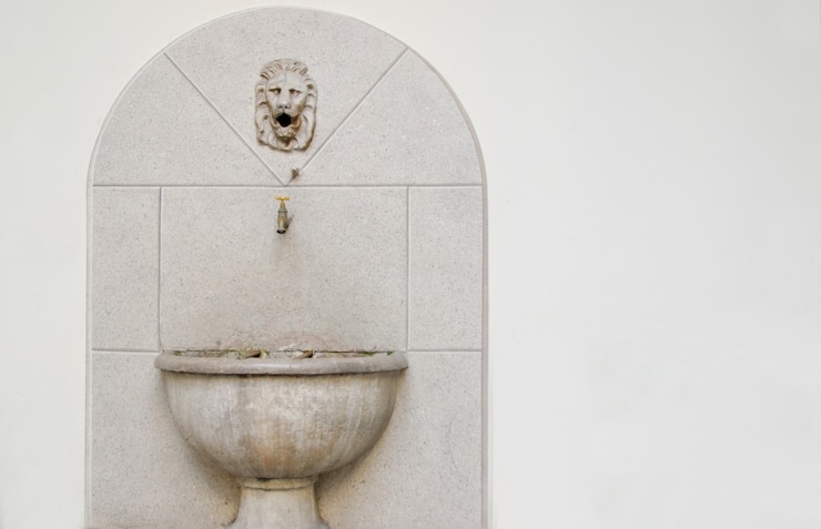 Foto gratuito vecchio lavello in pietra e una piccola gru con sopra una scultura di leone contro un bianco