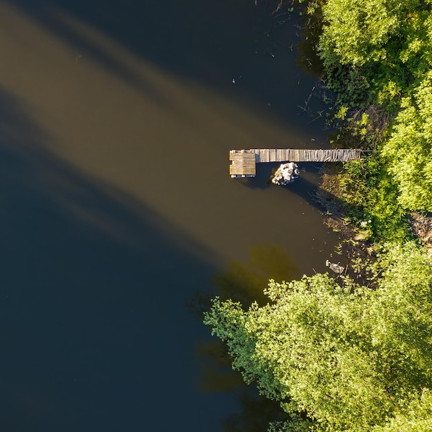 Veduta aerea di un lago soleggiato circondato da una pineta e da un ponte di legno Durante la soleggiata giornata estiva Foto di drone