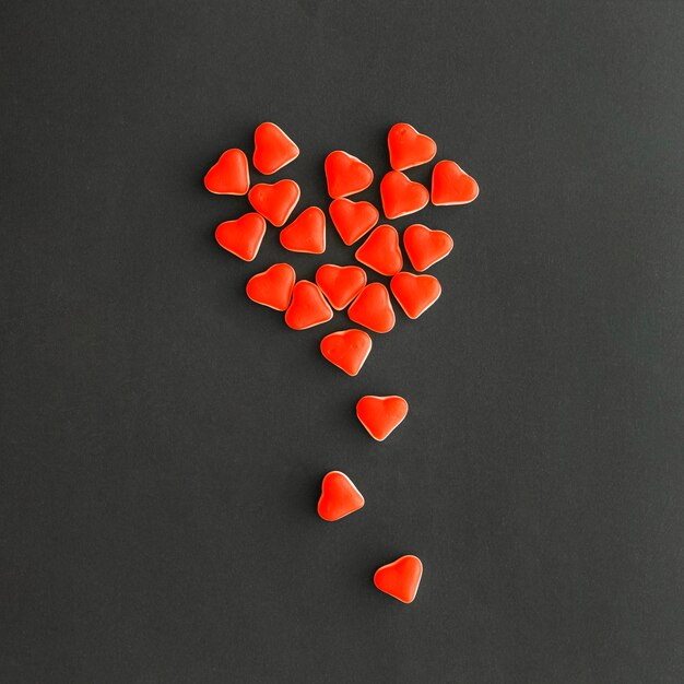 Veduta dall&#39;alto del design realizzato con piccole caramelle a forma di cuore rosso su sfondo nero