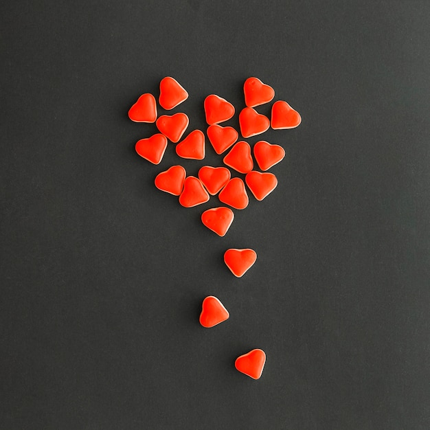 Veduta dall&#39;alto del design realizzato con piccole caramelle a forma di cuore rosso su sfondo nero