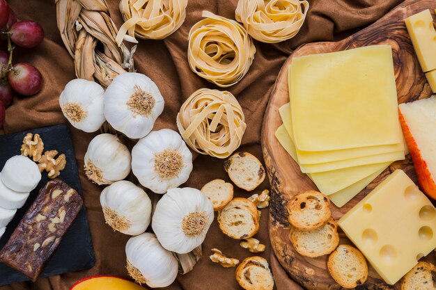 Veduta dall&#39;alto di bulbi di aglio, tipi di formaggio, pasta sul panno marrone