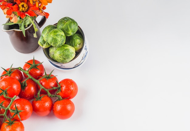 Veduta dall&#39;alto di pomodori succosi; cavoletti di Bruxelles e fiori su sfondo bianco