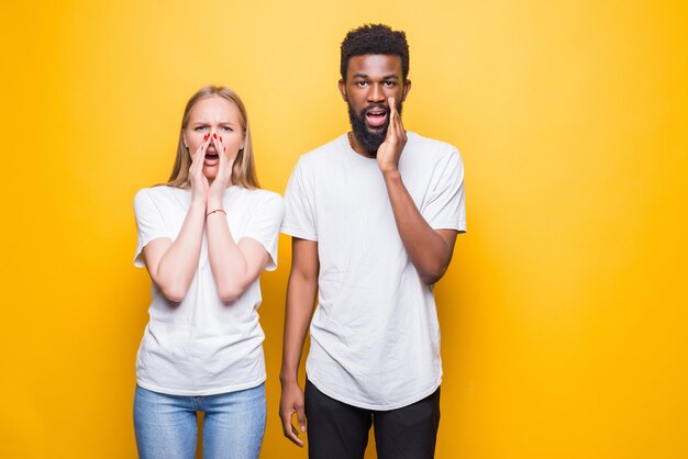 Vendite fantastiche. Coppia interrazziale scioccata che guarda di fronte e si tocca le guance con stupore, posando insieme isolati su un muro giallo