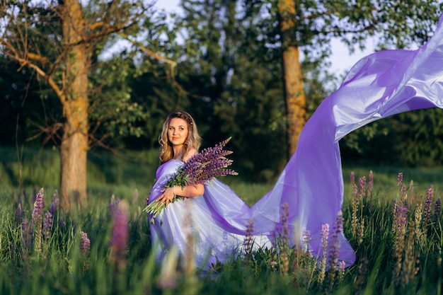 Vento soffia vestito viola donna incinta mentre lei sta nel campo di lavanda