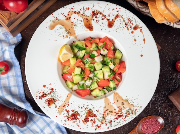 Verdura, pomodori, cetrioli, insalata di roka. insalata con sumakh e limone sul tavolo della cucina all&#39;interno del piatto bianco