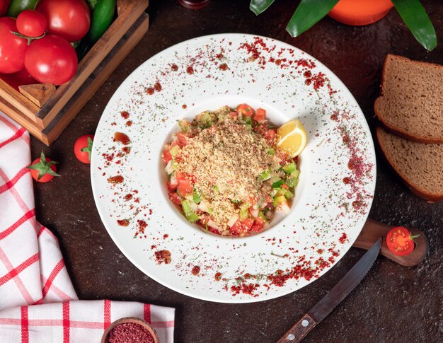 Verdura, pomodori, insalata di cetrioli con cracker. insalata sul tavolo della cucina con sumakh e limone all&#39;interno del piatto bianco