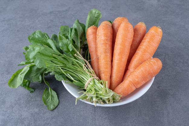 Verdura verde con carota su una ciotola, sulla superficie di marmo.