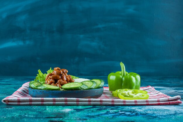 Verdure a fette e fagioli al forno su un piatto di legno su un asciugamano, sullo sfondo blu.