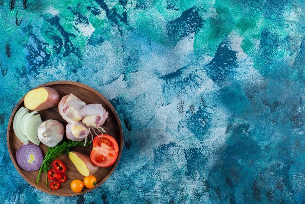 Verdure assortite e coscia di pollo su un piatto di legno, su sfondo blu.