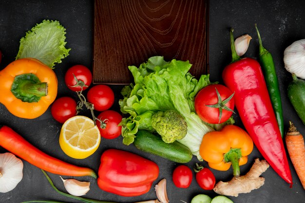 verdure come pomodoro lattuga pepe e altri con limone e tagliere sul tavolo nero