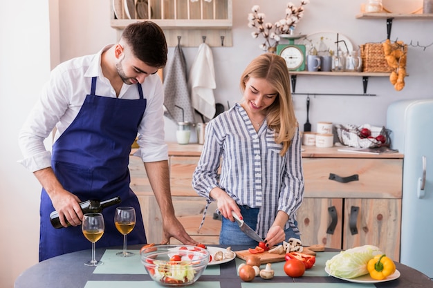 Verdure di taglio della donna mentre uomo che versa vino in vetro