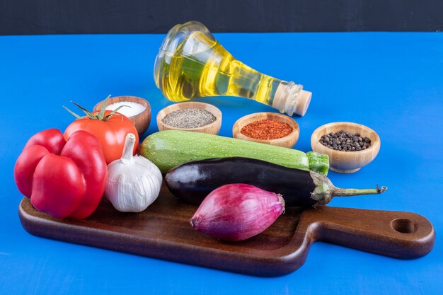 Verdure fresche su piatto di legno e bottiglia di olio d'oliva con spezie