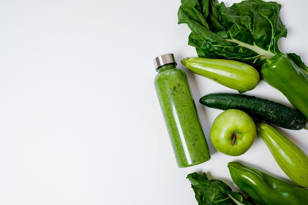 Verdure verdi e frullati in una bottiglia di plastica su sfondo bianco Concetto sano Vista dall'alto Spazio per il testo