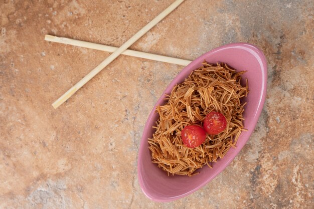 Vermicelli fritti con pomodoro in una ciotola rosa con le bacchette. Foto di alta qualità