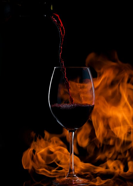 versando il vino rosso nel bicchiere con gambo lungo, con il fuoco in background