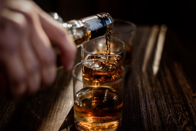 Versare una forte bevanda alcolica nei bicchieri che si trovano sul tavolo di legno
