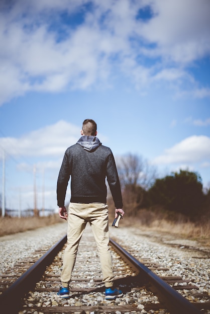 Verticale di un maschio che tiene la Bibbia mentre in piedi su un binario del treno con uno sfocato
