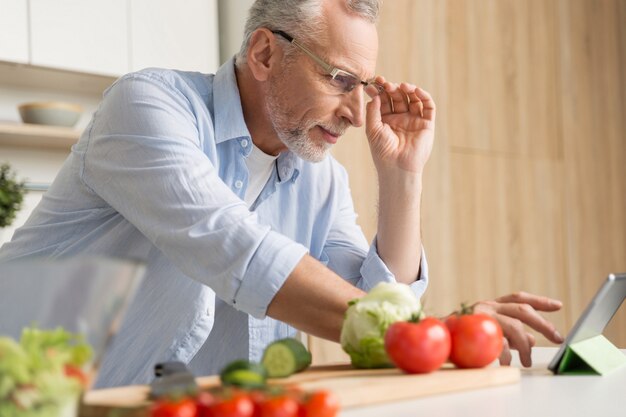 Vetri d'uso dell'uomo maturo bello che cucinano insalata