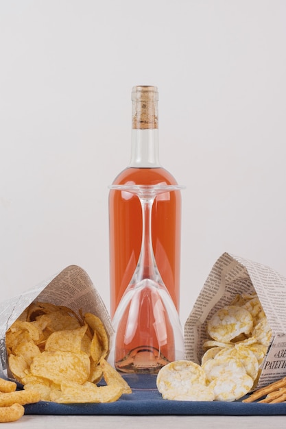 Vetro e bottiglia di vino rosato con vari snack sul tavolo bianco.