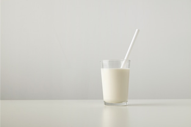 Vetro trasparente con latte biologico fresco e cannuccia bianca all'interno isolato sul lato del tavolo bianco