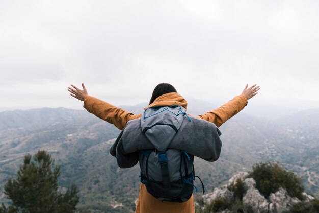 Viaggiatore con zaino e sacco a pelo femminile che sta sulla cima della montagna che ama la natura