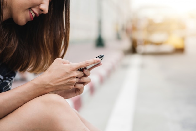 Viaggiatore con zaino e sacco a pelo turistico della donna asiatica che sorride e che usando smartphone che viaggia da solo